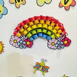 Decoração de arco-íris com flores coloridas e abelhas em sala de aula.