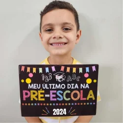 Criança sorridente segurando cartaz de despedida da pré-escola.