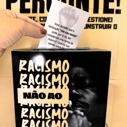 Pessoa colocando voto em urna com mensagem contra racismo.