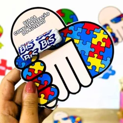 Mão segurando símbolo de autismo com quebra-cabeça colorido.