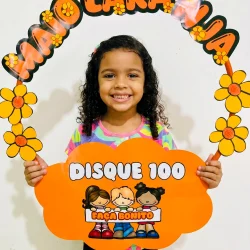 Criança sorridente com decoração de bambolê e flores laranja.