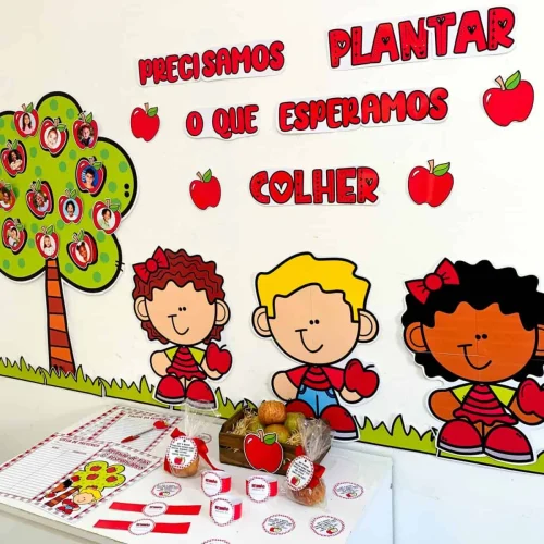 Crianças com maçãs de papel e cartaz educativo na parede.