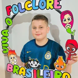 Menino segurando quadro com personagens folclóricos e palavras Folclore Brasileiro.