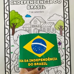 Criança segurando bandeira do Brasil na frente de cartaz escolar.