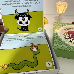 Livro com personagens do folclore brasileiro, Boi Bumbá e Boi Tatá, em caixa decorativa.