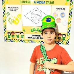 Criança com chapéu do Brasil e espada de papel na escola.
