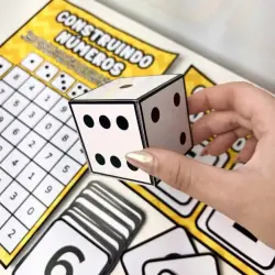 Pessoa segurando dado com números para ensino de matemática.