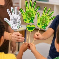 Mãos de crianças e adulto segurando mãos de papel com mensagens verdes.