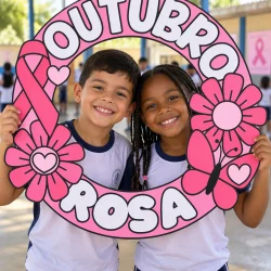 Crianças com sorriso segurando quadro Outubro Rosa na escola.